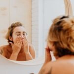 A woman gently washing her face in a bathroom mirror for her skincare routine.